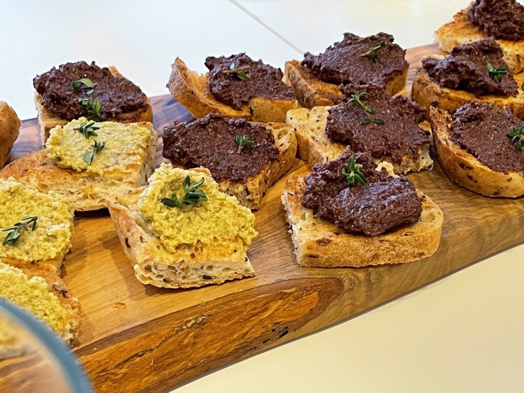 Glutenfreies Brot mit grüner und schwarzer Tapenade auf Olivenholzbrett